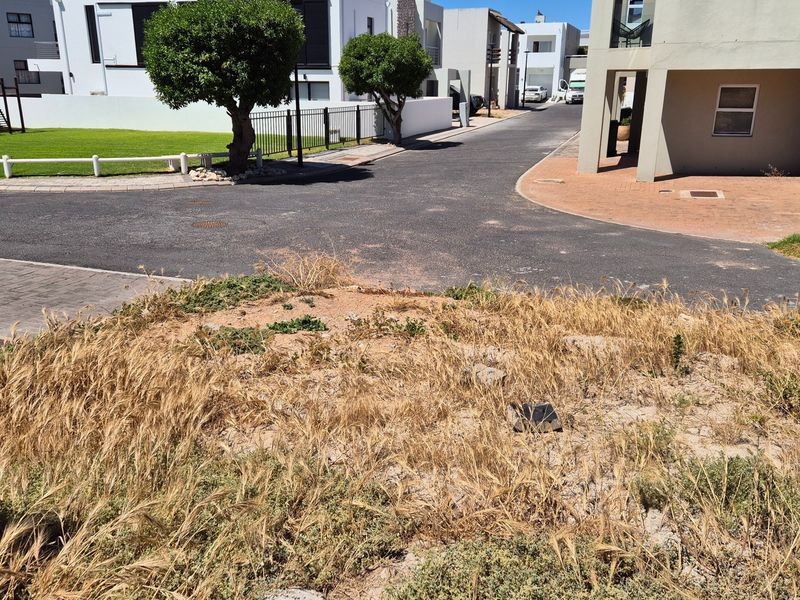 A view of an undeveloped residential plot situated within a developed estate, featuring surrounding paved roads and established neighbouring properties.