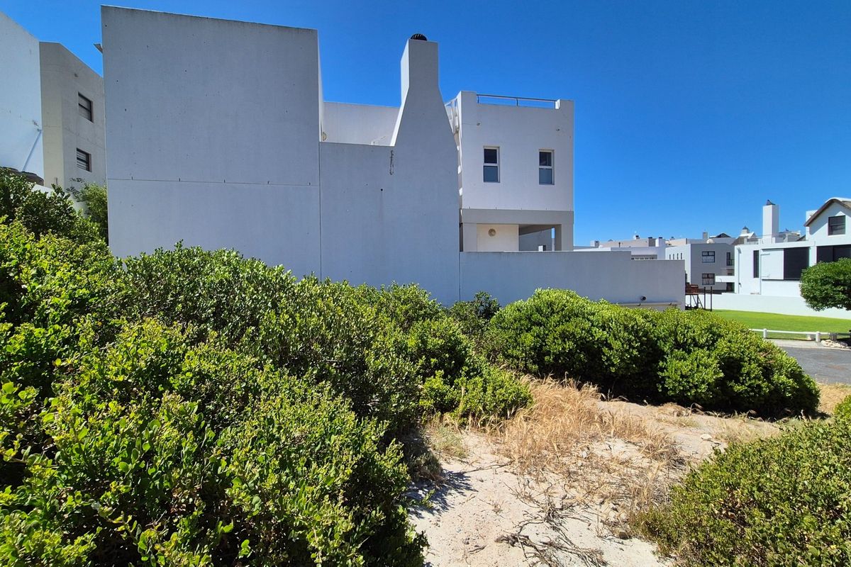 A view of the rear elevation of a white residential building featuring a chimney and balcony, set against a landscaped garden area.