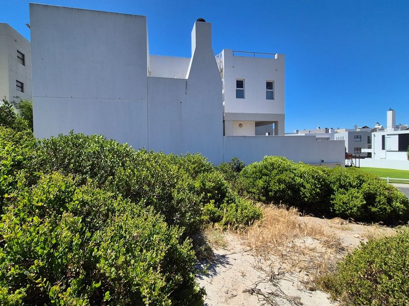 A view of the rear elevation of a white residential building featuring a chimney and balcony, set against a landscaped garden area.