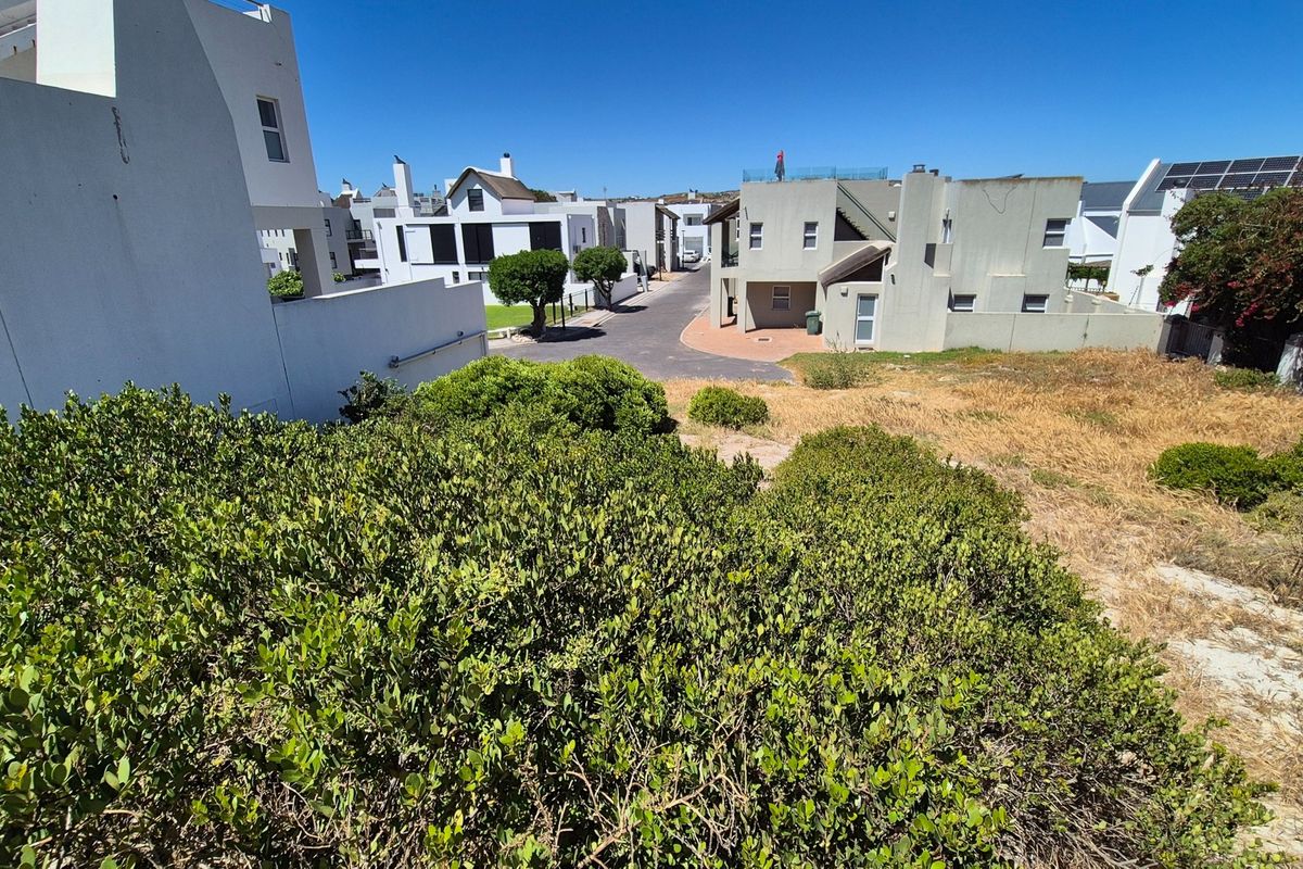 A view of a vacant residential plot situated within a developed neighborhood, featuring established shrubbery and proximity to existing residential properties.