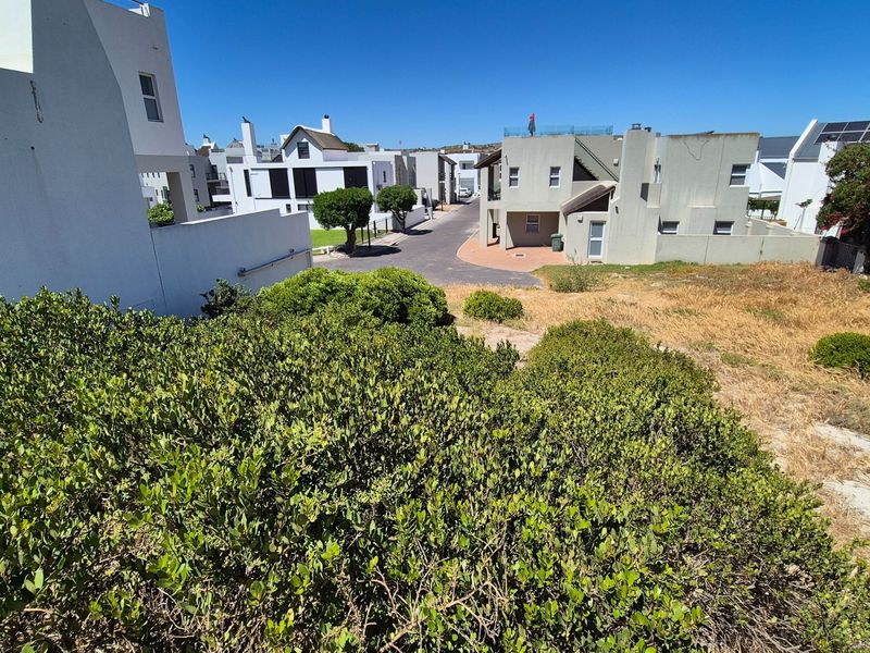 A view of a vacant residential plot situated within a developed neighborhood, featuring established shrubbery and proximity to existing residential properties.