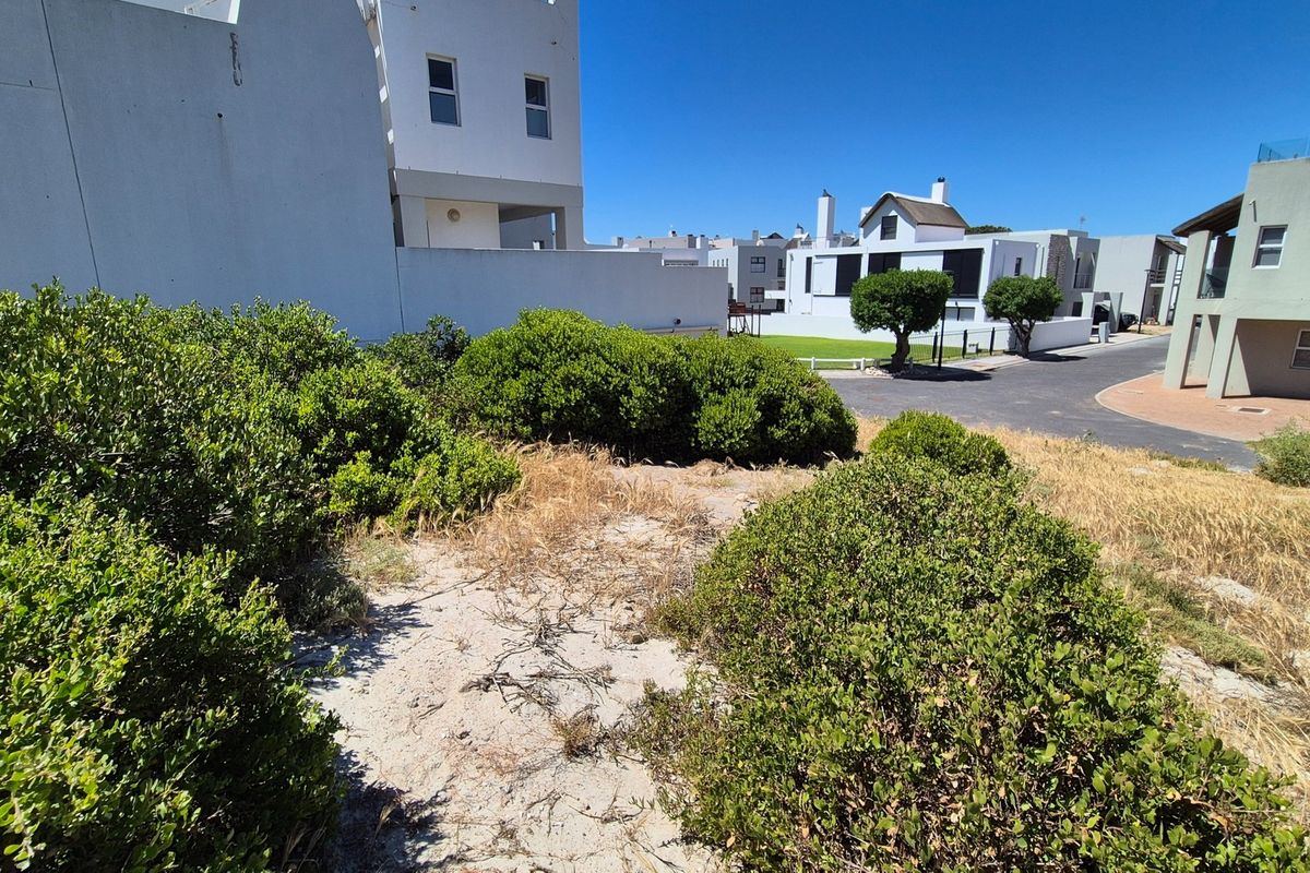 A view of a vacant residential plot featuring established shrubs and direct access to a paved street in a developed neighborhood.