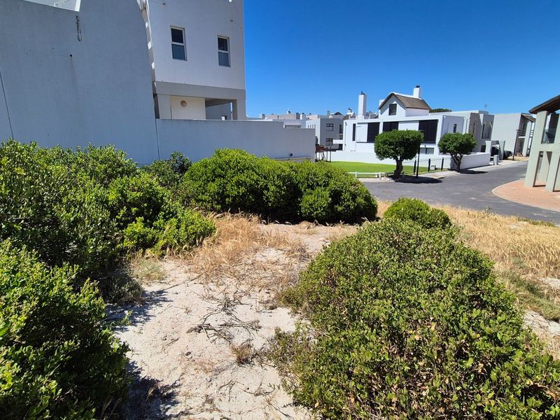 A view of a vacant residential plot featuring established shrubs and direct access to a paved street in a developed neighborhood.