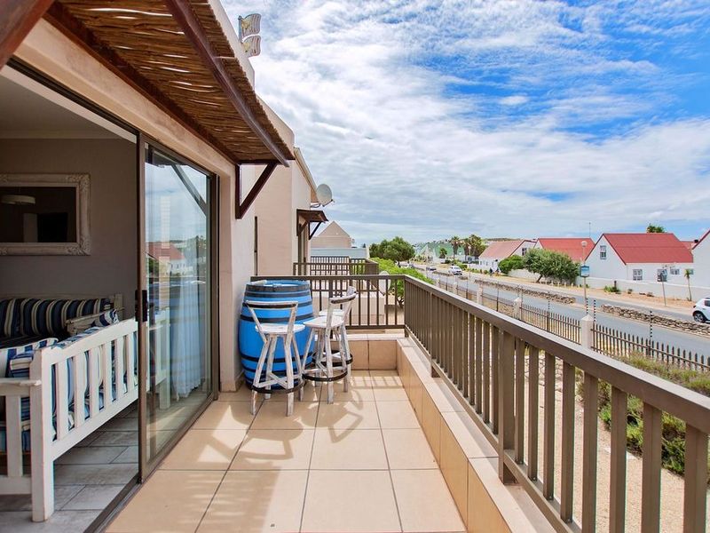 A spacious balcony featuring tiled flooring, a protective railing, and a thatched roof overhang, offering an outdoor space accessible via sliding glass doors.