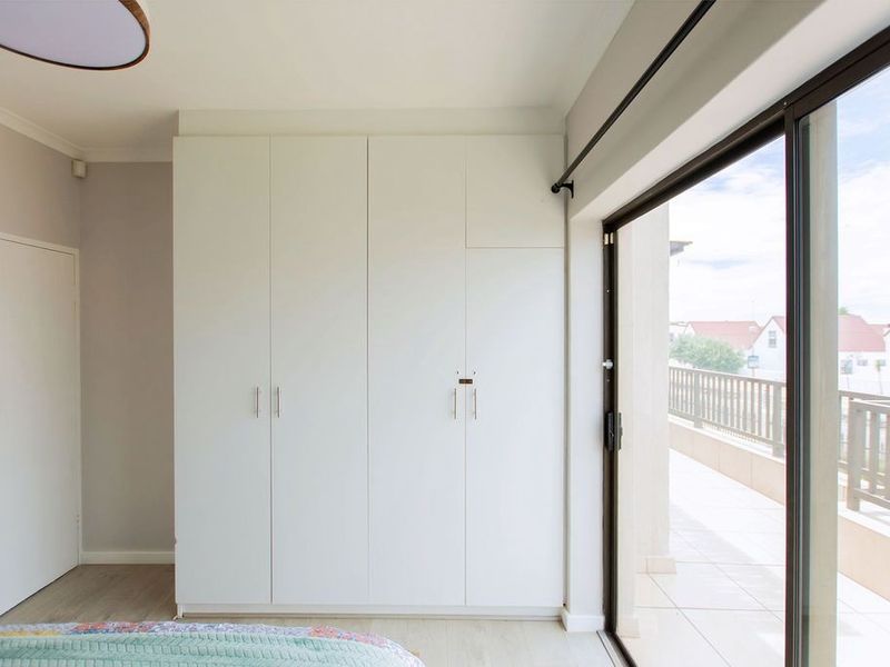 A bright bedroom featuring modern built-in cupboards and a large sliding glass door providing direct access to a private balcony.