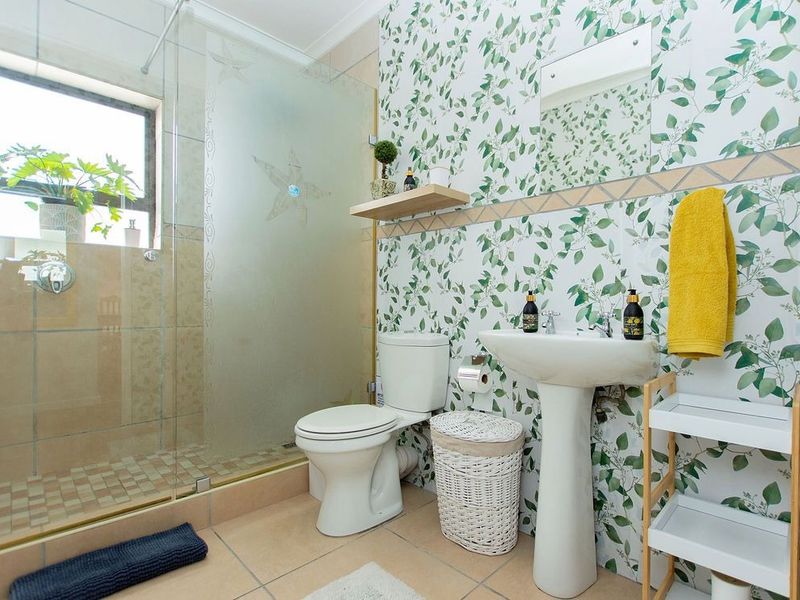 A functional bathroom featuring a pedestal sink, toilet, and a glass-enclosed shower with decorative tiled walls and flooring.