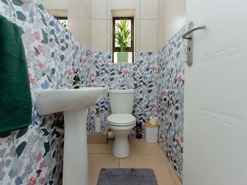 A compact bathroom featuring a pedestal basin, toilet, and decorative floral-patterned wall tiles.