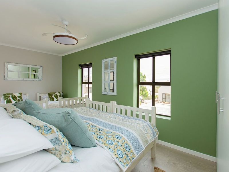A well-maintained bedroom featuring laminate flooring, a ceiling fan, and a built-in wardrobe, finished with a modern green accent wall.