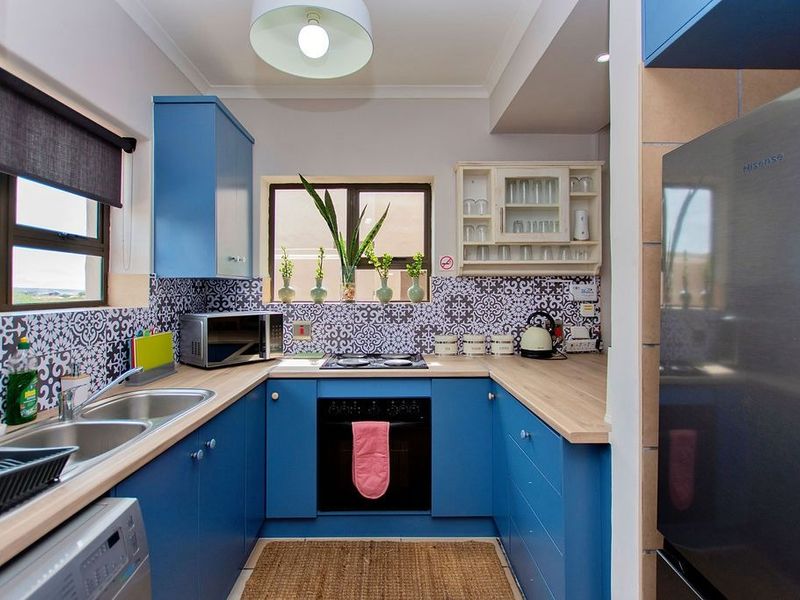 A compact, well-maintained kitchen featuring vibrant blue cabinetry, patterned tile backsplash, laminate countertops, and integrated cooking appliances.