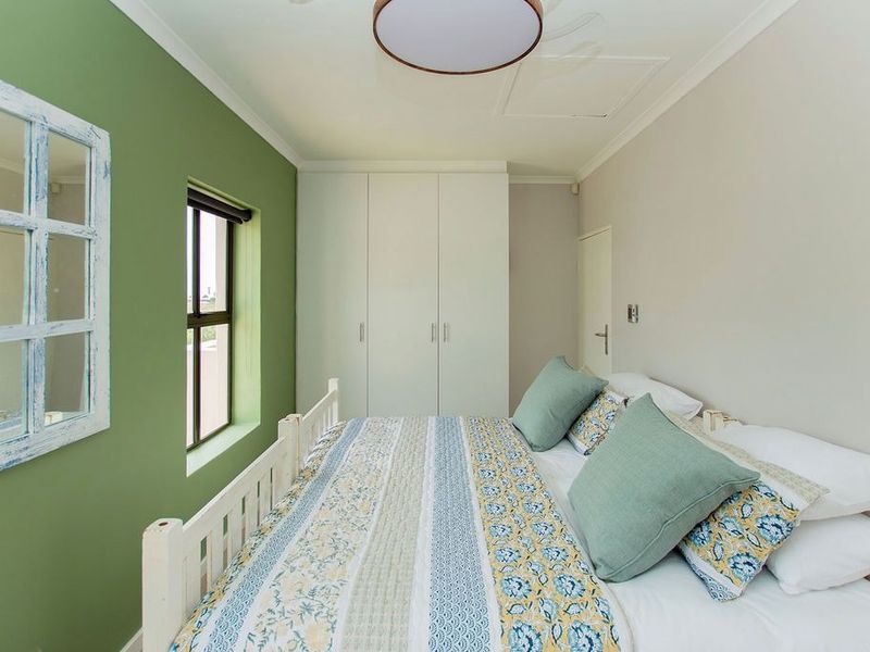 A well-maintained bedroom featuring built-in cupboards, a ceiling fan, and a window with a green accent wall.