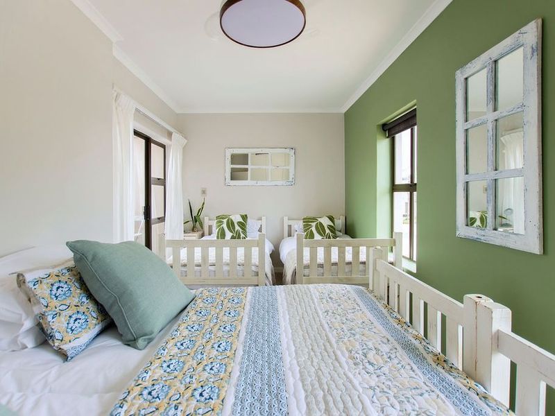 A well-lit bedroom featuring a green accent wall, large windows, and a sliding glass door providing access to an outdoor area.