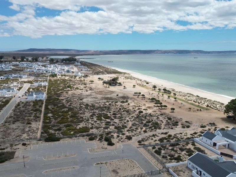 Aerial view of a coastal residential estate featuring proximity to the beach, natural landscape, and paved parking infrastructure.
