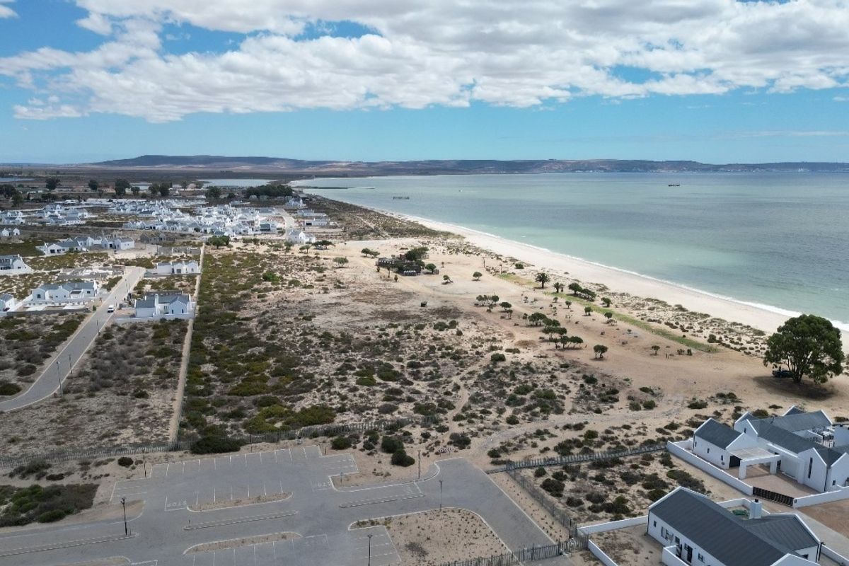 Aerial view of a coastal residential estate featuring proximity to the beach, natural landscape, and paved parking infrastructure.