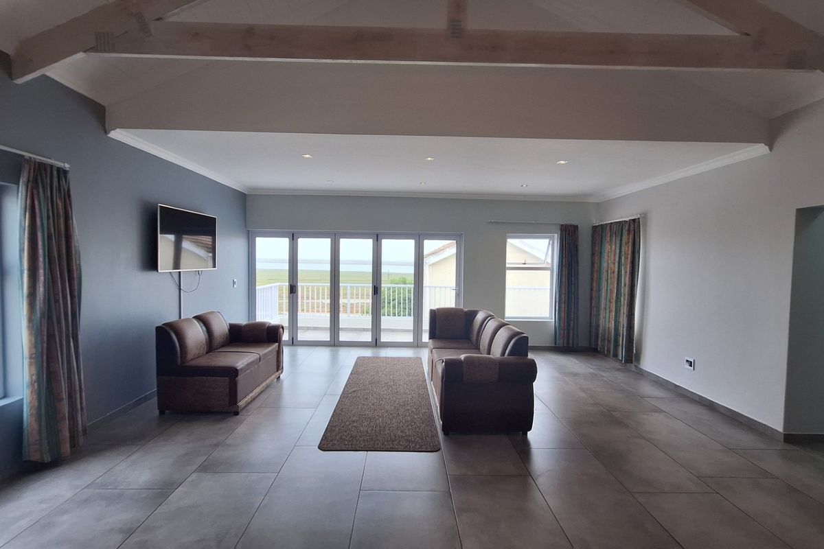 Spacious living room featuring vaulted ceilings with exposed timber beams, large format floor tiles, and bi-fold doors opening to an outdoor balcony area.