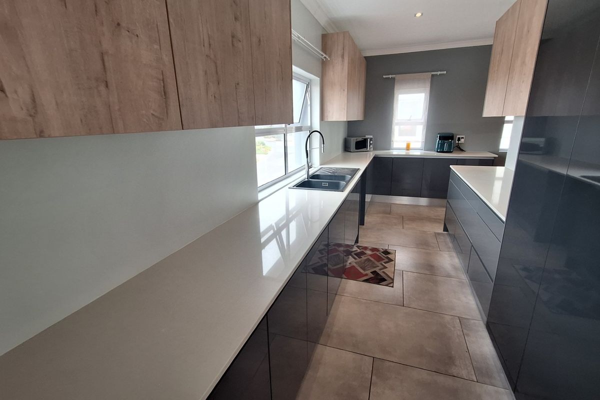 Modern kitchen featuring sleek dark grey and wood-tone cabinetry, stone countertops, and large format floor tiles in a clean, contemporary layout.