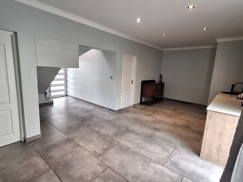 Spacious open-plan living area featuring large format floor tiles, recessed downlighting, and a functional kitchen corner with built-in cabinetry.