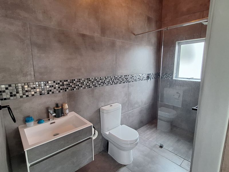 Modern bathroom featuring large format grey wall tiles, a mosaic accent border, a floating vanity, and a walk-in shower with a glass screen.