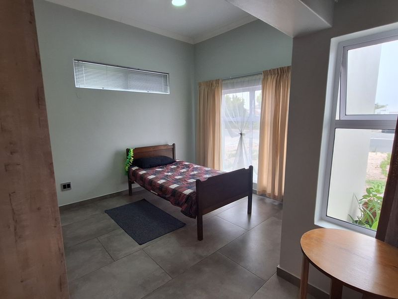 A well-lit bedroom featuring neutral tiled flooring, modern aluminium window frames, and a combination of horizontal blinds and curtains.