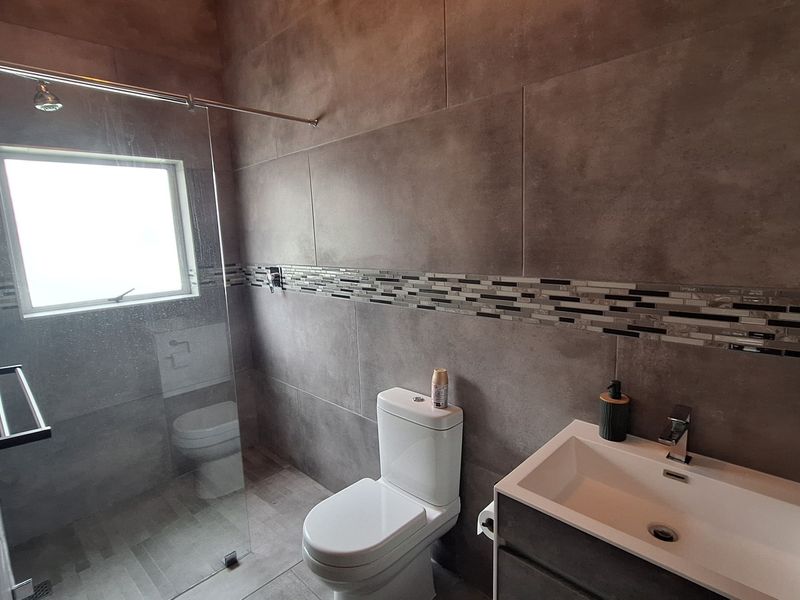 Modern bathroom featuring large format grey wall tiles, a glass shower enclosure, a contemporary vanity basin, and a sleek toilet.