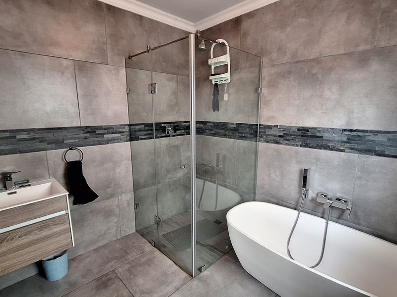 Modern bathroom featuring a freestanding bathtub, a glass-enclosed shower, and a wall-mounted vanity with contemporary grey tiling throughout.