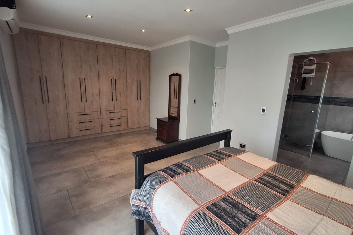 Spacious bedroom featuring extensive built-in cabinetry, tiled flooring, recessed lighting, and direct access to a modern en-suite bathroom with a freestanding tub and shower.