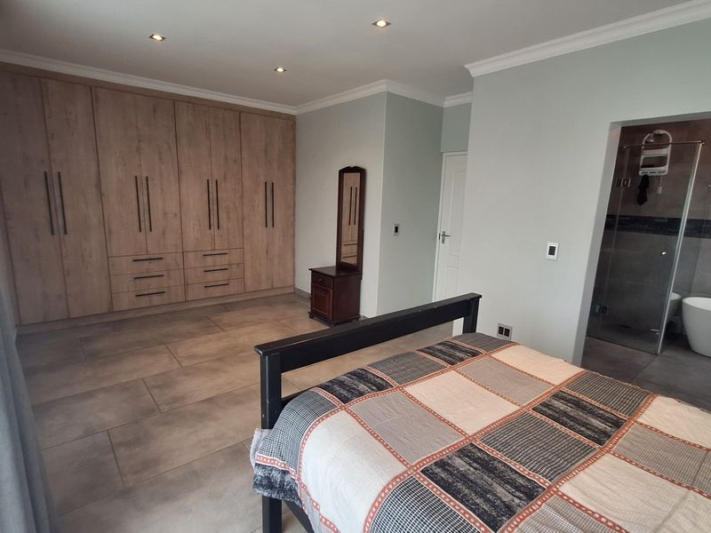 Spacious bedroom featuring extensive built-in cabinetry, tiled flooring, recessed lighting, and direct access to a modern en-suite bathroom with a freestanding tub and shower.
