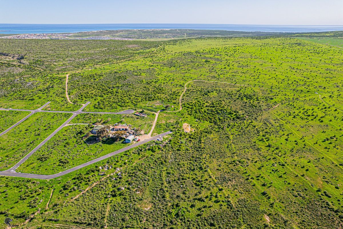 An aerial view of a large, undeveloped residential land parcel featuring established paved road access and expansive natural vegetation.