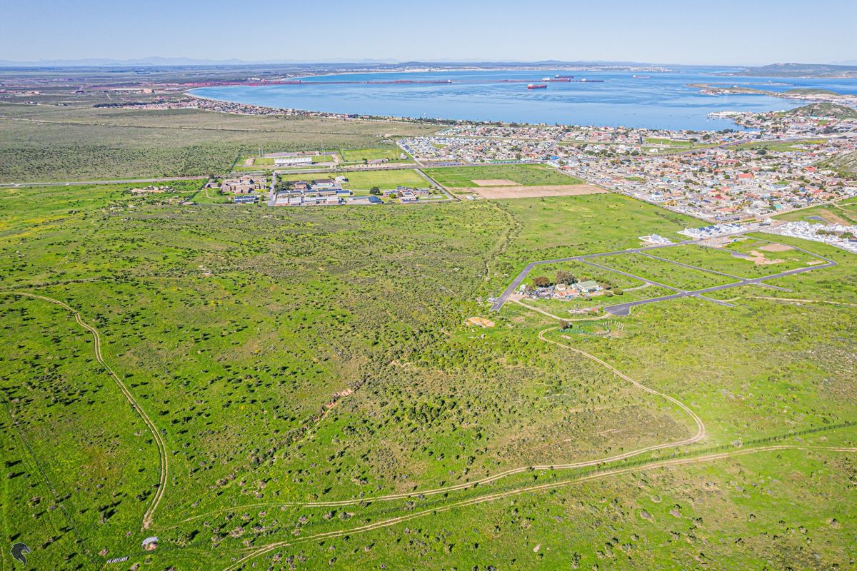 An aerial view of a large, undeveloped residential land parcel featuring natural vegetation, dirt tracks, and proximity to the coastline and urban infrastructure.
