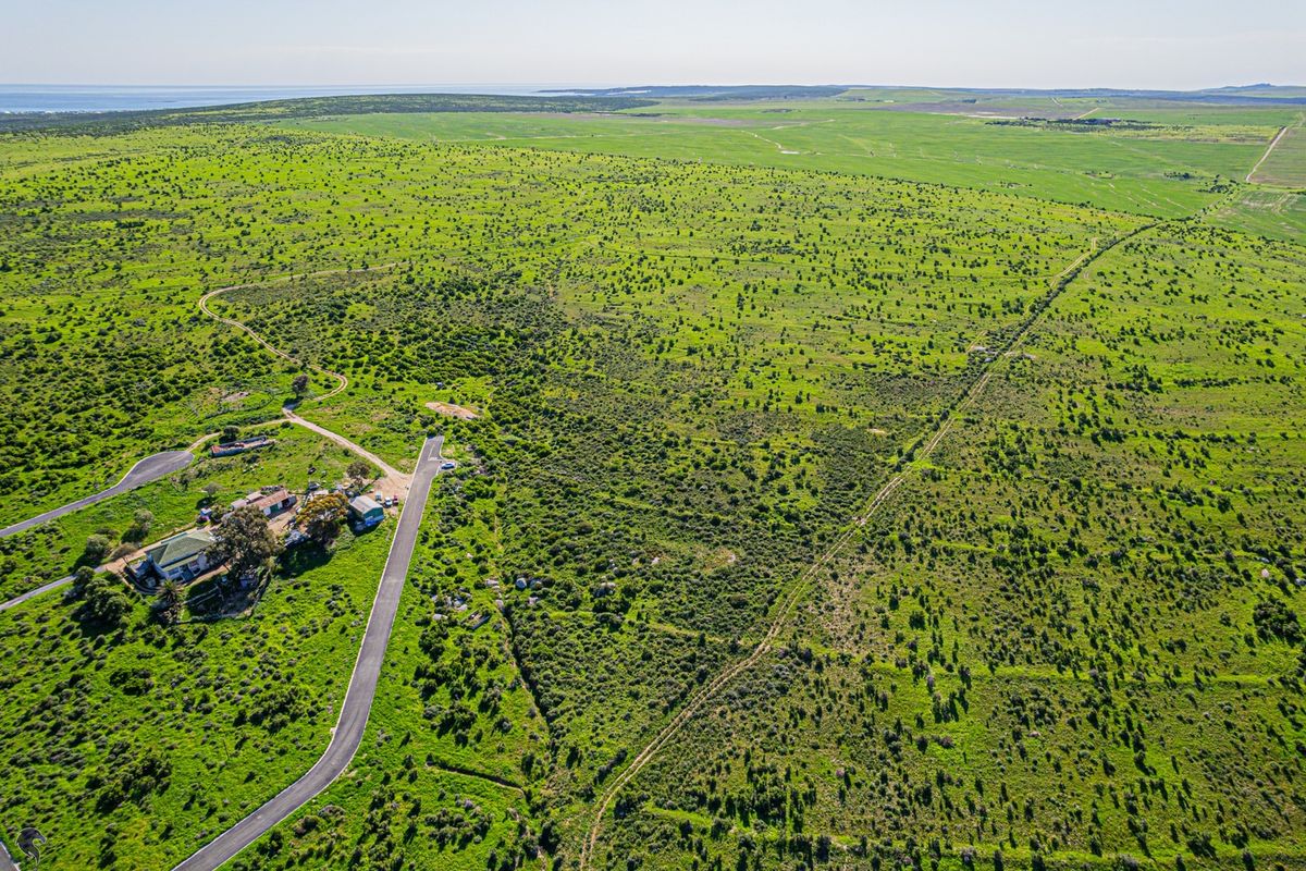 Aerial view of a large, expansive vacant residential land parcel featuring existing structures and paved road access, surrounded by natural green landscape.