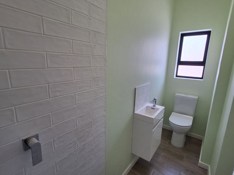 A modern, clean guest bathroom featuring a wall-mounted vanity, basin, toilet, and stylish subway tile accents.