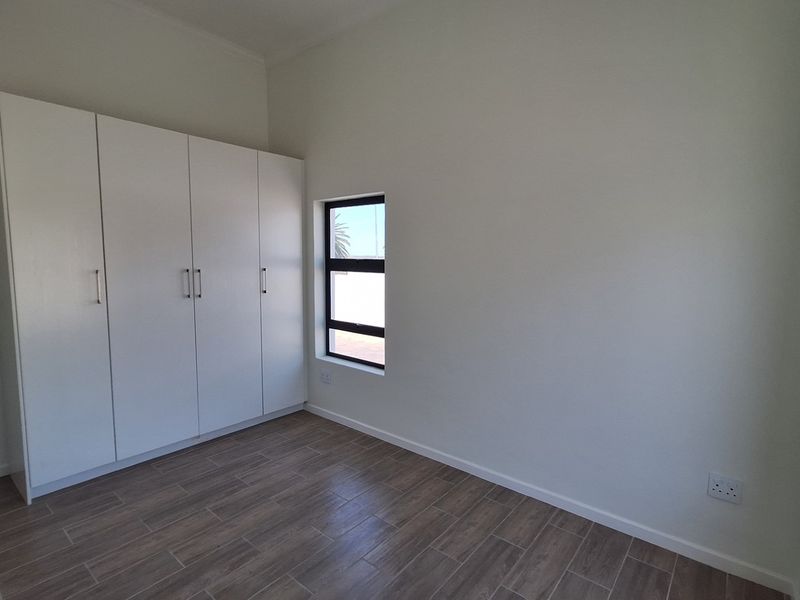 A bright, modern bedroom featuring neutral walls, wood-look tiled flooring, and ample built-in cupboard storage.