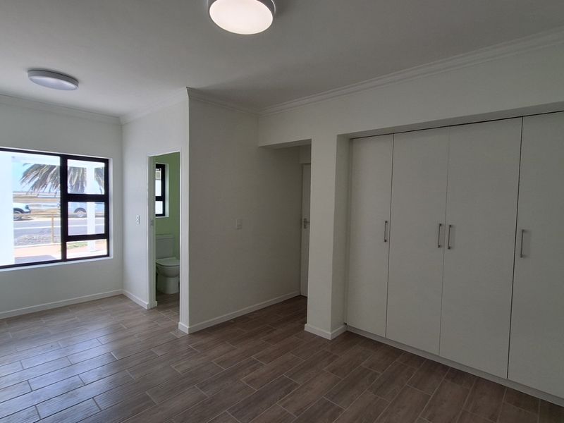 A bright, empty bedroom featuring modern wood-look tiled flooring, built-in cupboards, and an en-suite bathroom access.