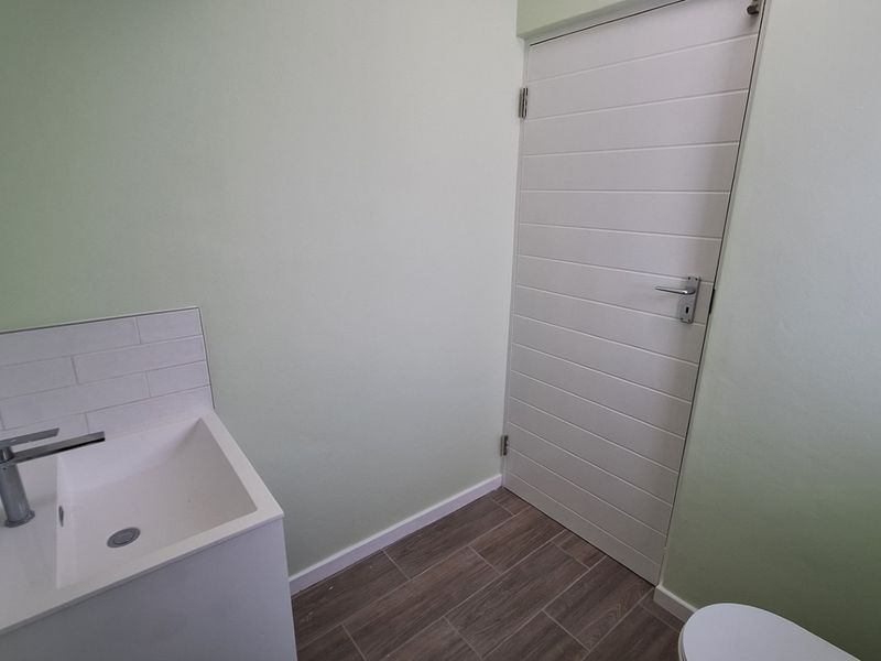 A clean, minimalist bathroom featuring a modern basin with tiled splashback, wood-look tiled flooring, and a white internal door.