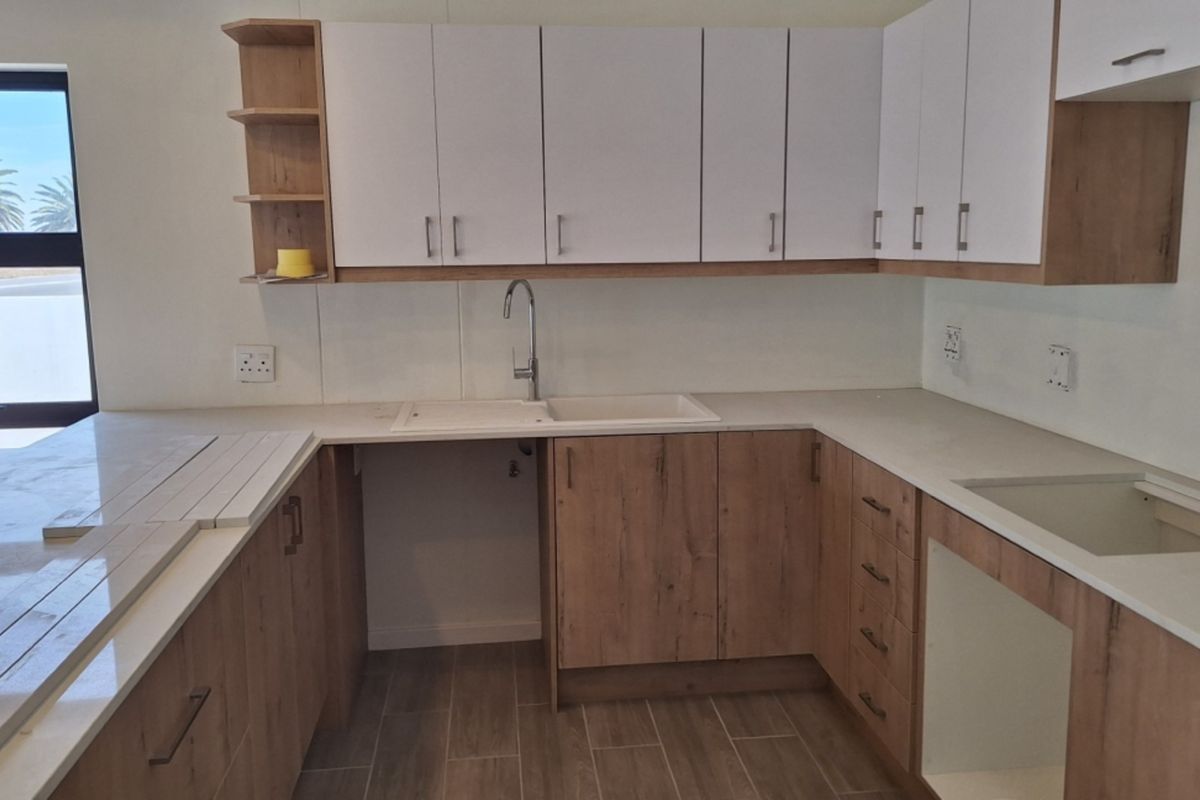A modern, empty kitchen featuring light wood-tone cabinetry, white countertops, and tiled flooring, offering a clean and functional space ready for appliances.