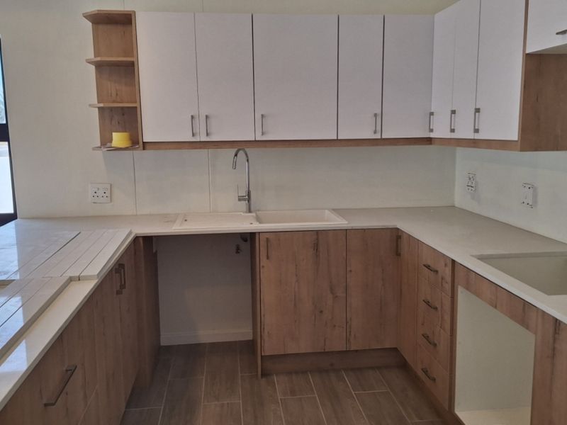 A modern, empty kitchen featuring light wood-tone cabinetry, white countertops, and tiled flooring, offering a clean and functional space ready for appliances.