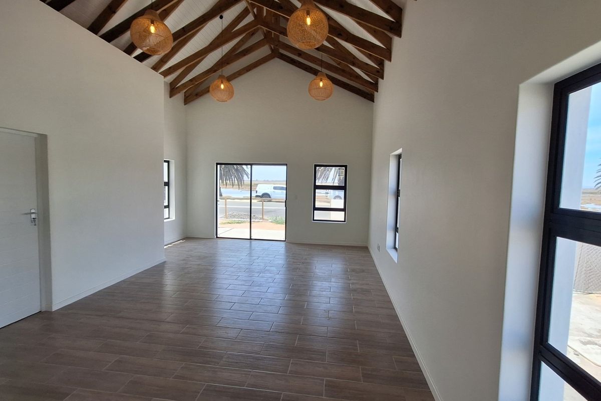 Spacious living area featuring high vaulted ceilings with exposed timber trusses, modern tiled flooring, and large aluminium-framed windows and sliding doors.