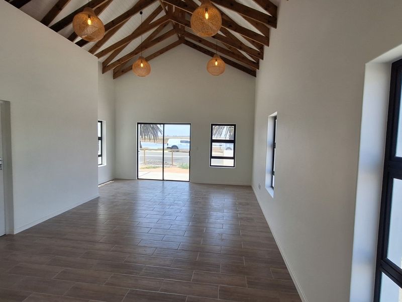 Spacious living area featuring high vaulted ceilings with exposed timber trusses, modern tiled flooring, and large aluminium-framed windows and sliding doors.