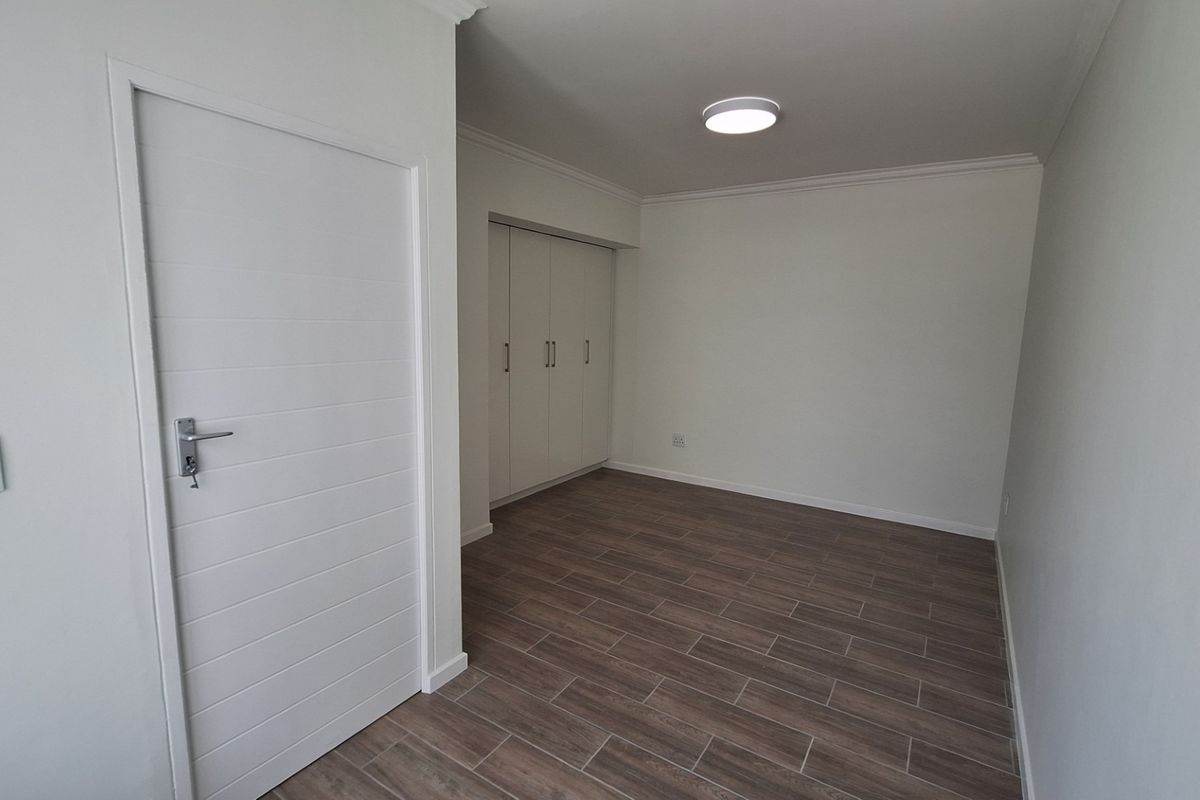 A clean, empty bedroom featuring modern wood-look tiled flooring, built-in cupboards, and neutral wall finishes, ready for personalization.