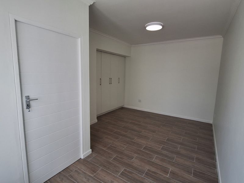 A clean, empty bedroom featuring modern wood-look tiled flooring, built-in cupboards, and neutral wall finishes, ready for personalization.