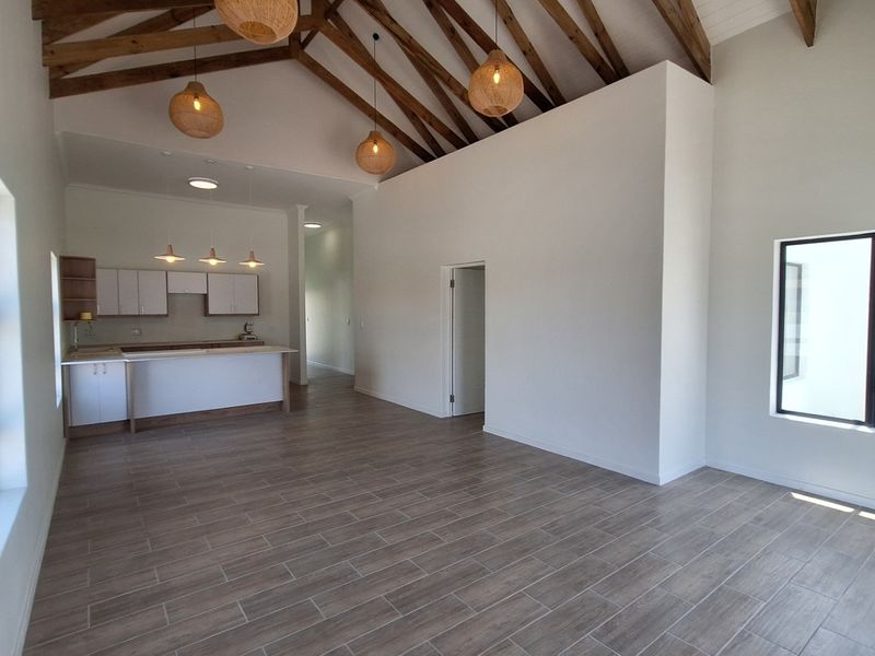 Spacious open-plan living area featuring high vaulted ceilings with exposed timber trusses, modern tiled flooring, and a contemporary kitchen with island cabinetry.