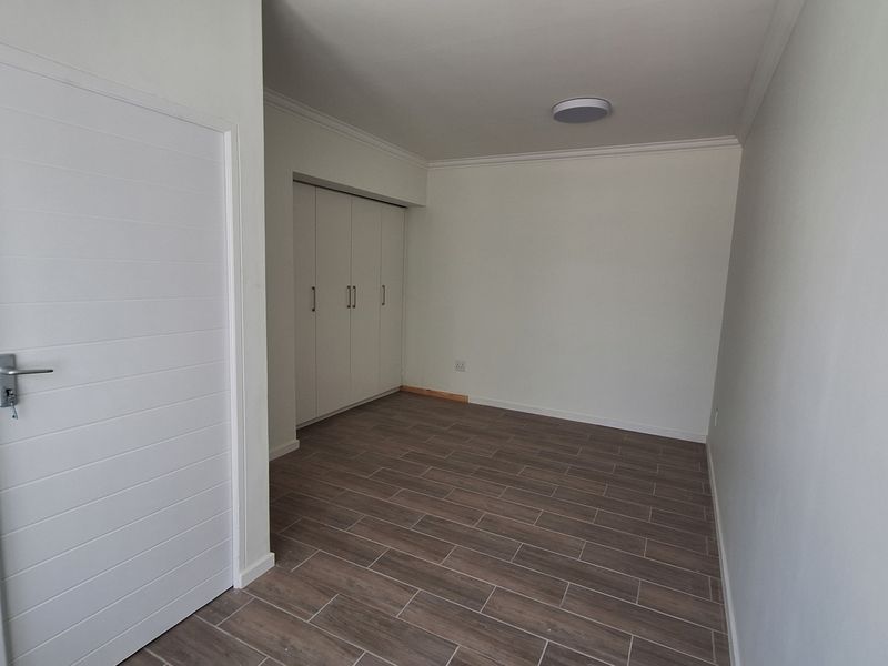 A clean, empty bedroom featuring modern wood-look tiled flooring, built-in cupboards, and neutral wall finishes, ready for personalization.