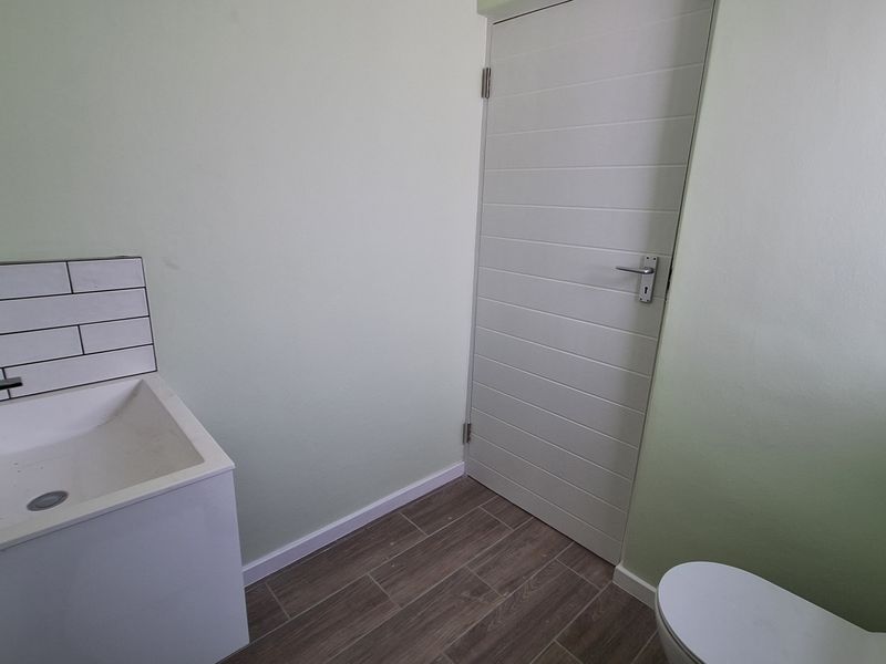 A clean, modern bathroom featuring a vanity basin with subway tile splashback, tiled flooring, and a white internal door.