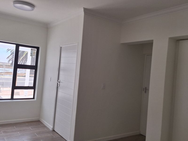A bright, empty bedroom featuring tiled flooring, built-in cupboards, and a large window with views, finished with clean white walls and ceiling cornices.