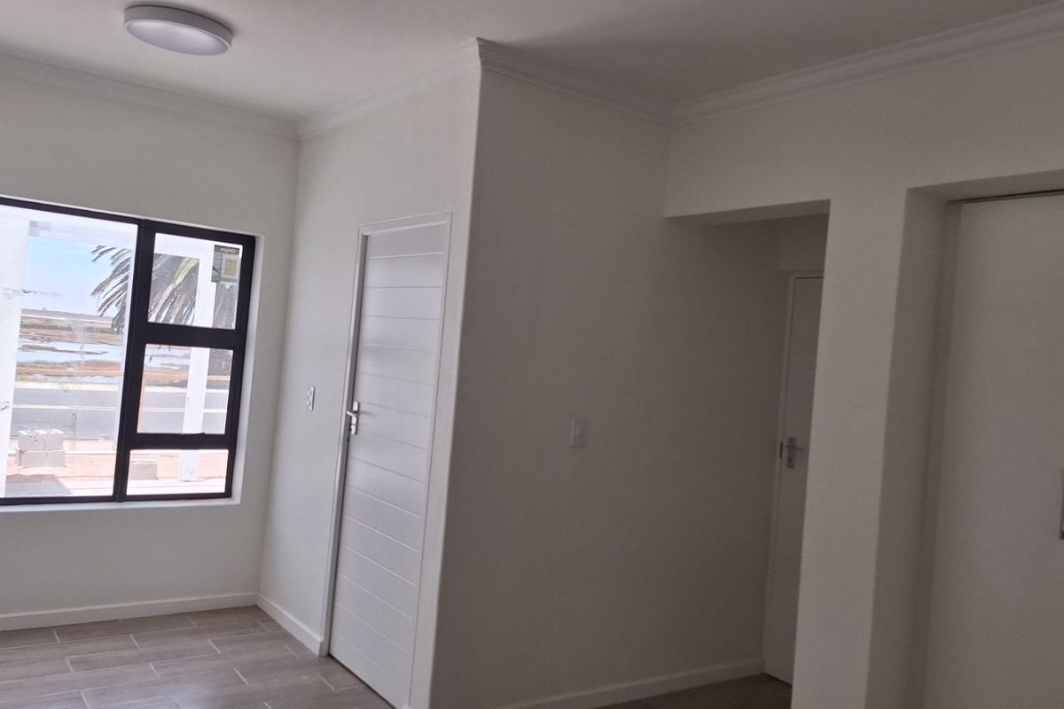 A bright, empty bedroom featuring tiled flooring, built-in cupboards, and a large window with views, finished with clean white walls and ceiling cornices.