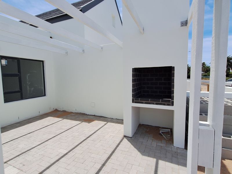 An outdoor patio area featuring a built-in brick braai, white pergola structure, and paved flooring, currently in an unfinished state.
