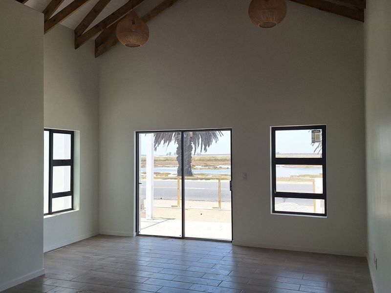 Spacious living area featuring a high vaulted ceiling with exposed timber rafters, tiled flooring, and large windows providing natural light and scenic views.