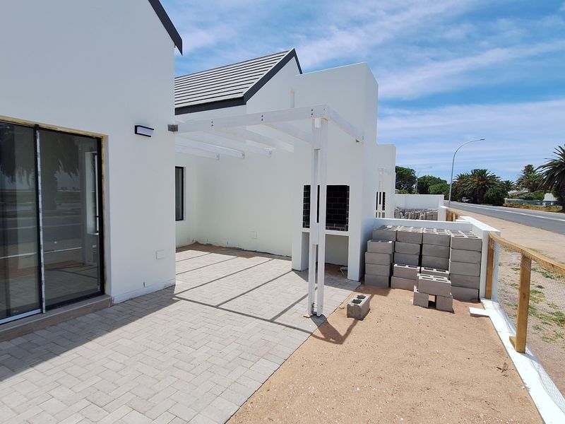 Outdoor patio area featuring a built-in braai, pergola structure, and paved flooring, adjacent to the main living area with sliding door access.