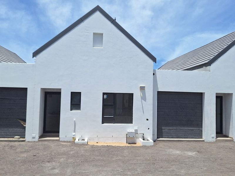 Front elevation of a modern townhouse complex featuring white rendered walls, dark tiled roofs, and integrated garage doors with unfinished ground area.