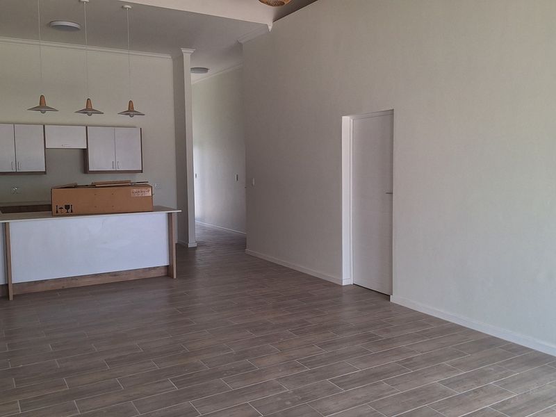 Spacious open-plan living area featuring a modern kitchen with island, neutral finishes, and tiled flooring throughout, offering a clean and versatile layout.