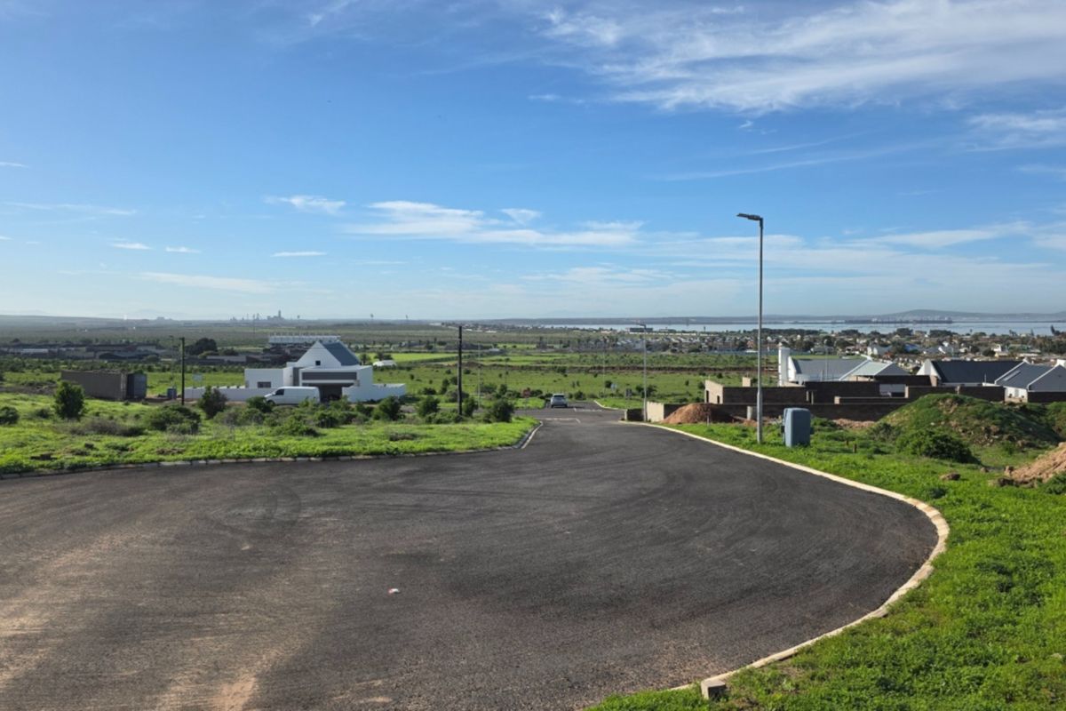 A wide-angle view of a residential development area featuring paved roads, street lighting, and surrounding landscape with distant coastal views.